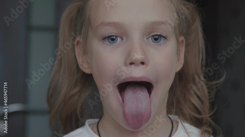 Child girl opens her mouth wide. child shows her teeth and mouth to dentist. mouth is wide open, tongue is stuck out as far as possible, with clear view of tongue and soft palate