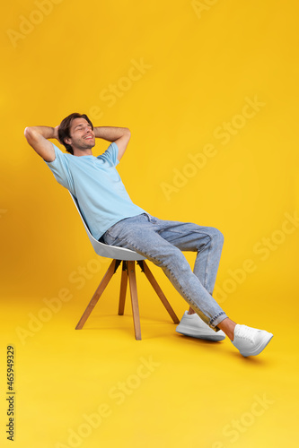 Happy guy relaxing sitting on chair, leaning back at studio