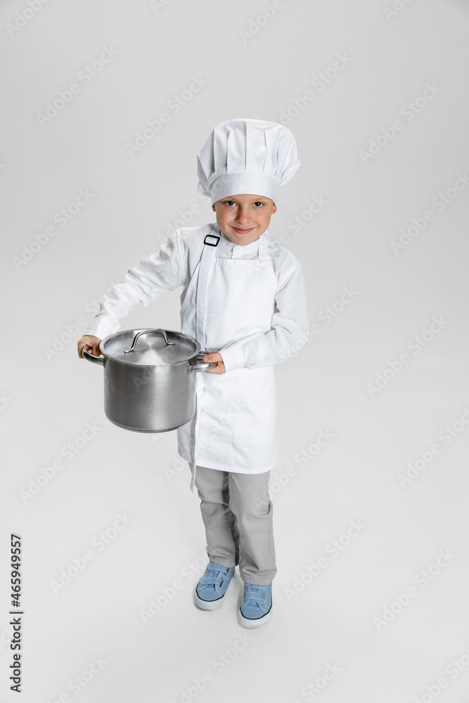 Portrait of little happy boy in white cook, chef jacket and hat standing isolated on white studio background. Portrait of little happy boy in white cook, chef jacket and hat standing isolated on white studio background.