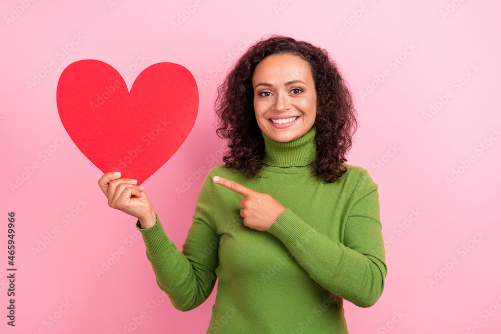 Photo of sweet charming african lady dressed green turtleneck smiling pointing finger large paper heart isolated pink color background Photo of sweet charming african lady dressed green turtleneck smiling pointing finger large paper heart isolated pink color background