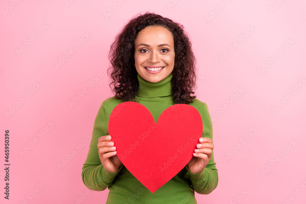 Photo of adorable dreamy afro woman wear green turtleneck holding big red heart smiling isolated pink color background