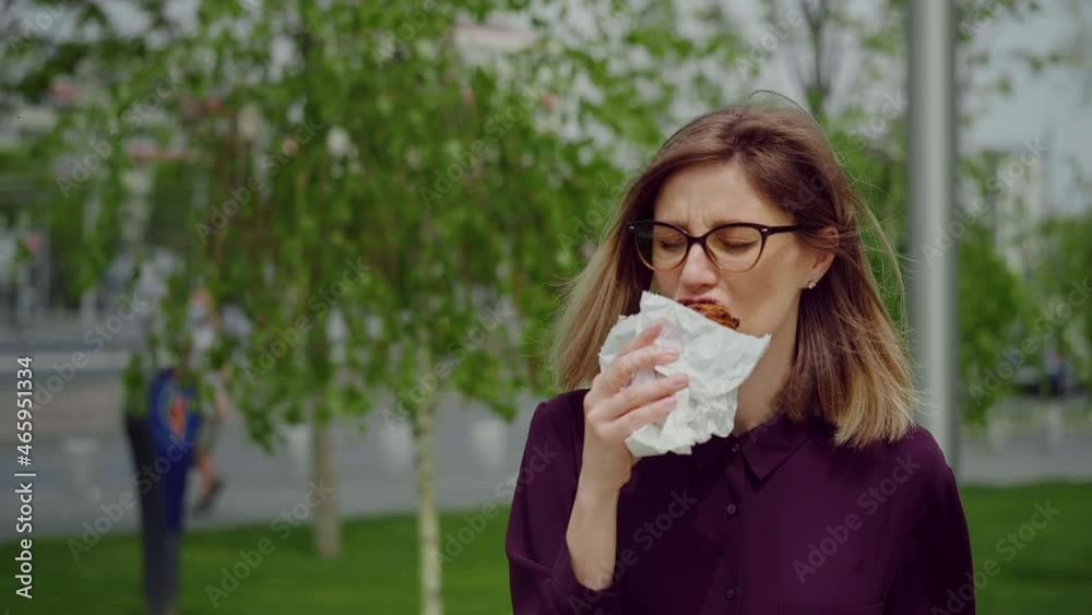 Young Female Walks and eating. Happy with Foo. Street Food in Park. Hungry business woman. Young Female Walks and eating. Happy with Foo. Street Food in Park. Hungry business woman.