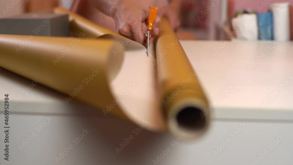 Close-up front view of unrecognizable young woman cutting with scissors wrapping golden paper to package festive cardboard box with Christmas present, selective focus. Concept of new year and xmas.