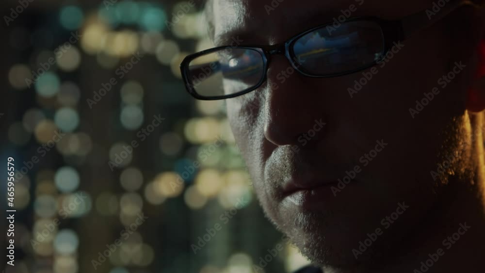 Close-up portrait of a young man working at the computer. Laptop display is reflected in glasses. Night city lights on the background. Business, coding and exchange concept. Close-up portrait of a young man working at the computer. Laptop display is reflected in glasses. Night city lights on the background. Business, coding and exchange concept.