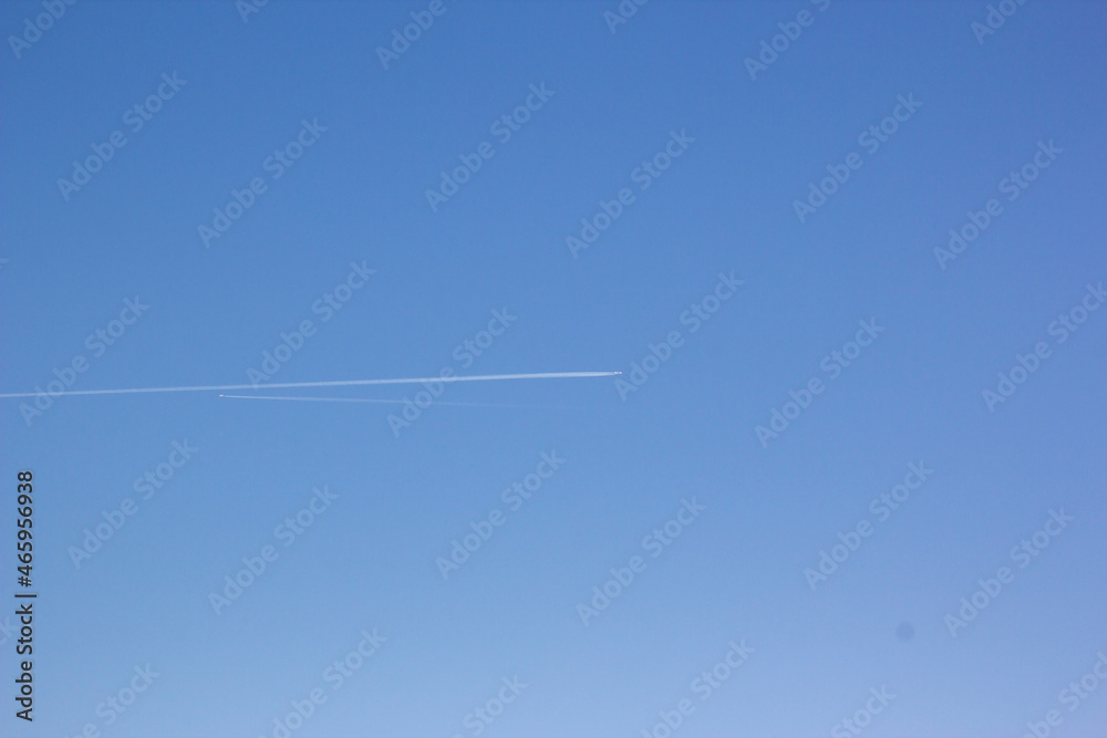 Inversion trail of clouds from the plane against the blue sky. Airplane leaving vapor trail behind. Track in the sky from a jet plane. Concept of planning routes and direction of travels Inversion trail of clouds from the plane against the blue sky. Airplane leaving vapor trail behind. Track in the sky from a jet plane. Concept of planning routes and direction of travels