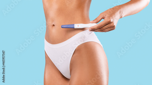 Woman holding positive pregnancy test wearing white underwear