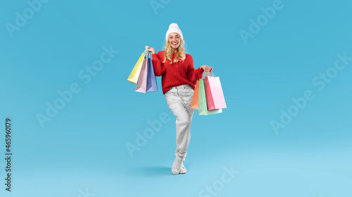 Smiling woman in winter hat holding shopping bags at studio