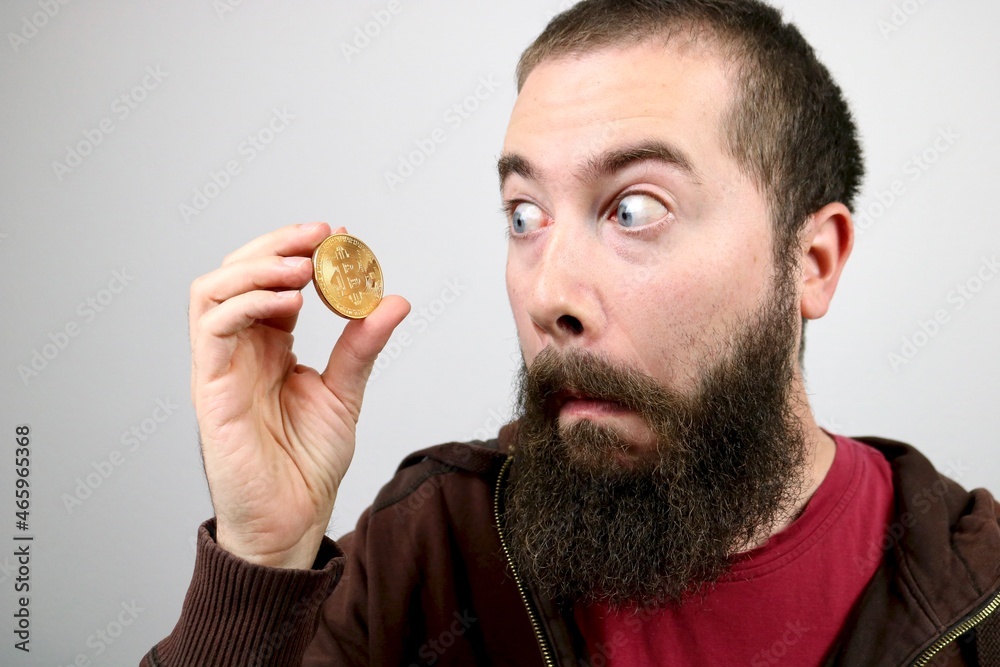 Young hipster man with beard looking at bitcoin Young hipster man with beard looking at bitcoin