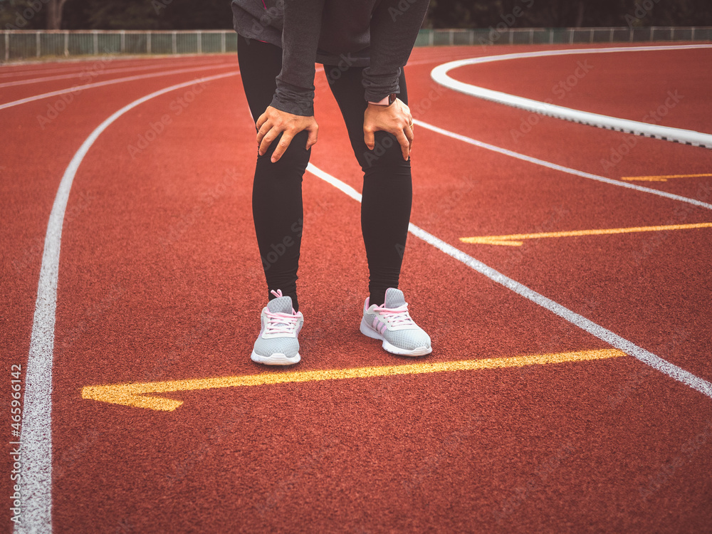 Tired female runner taking a rest after running hard on stadium track. Workout Healthy lifestyle concept.