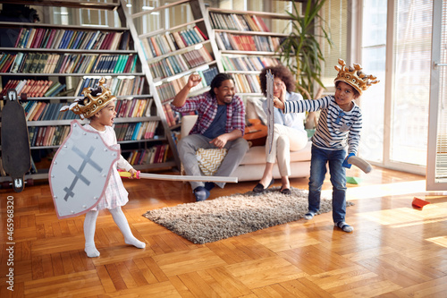 Young parents enjoying while kids are playing with swords at home. Family, together, love, playtime photo