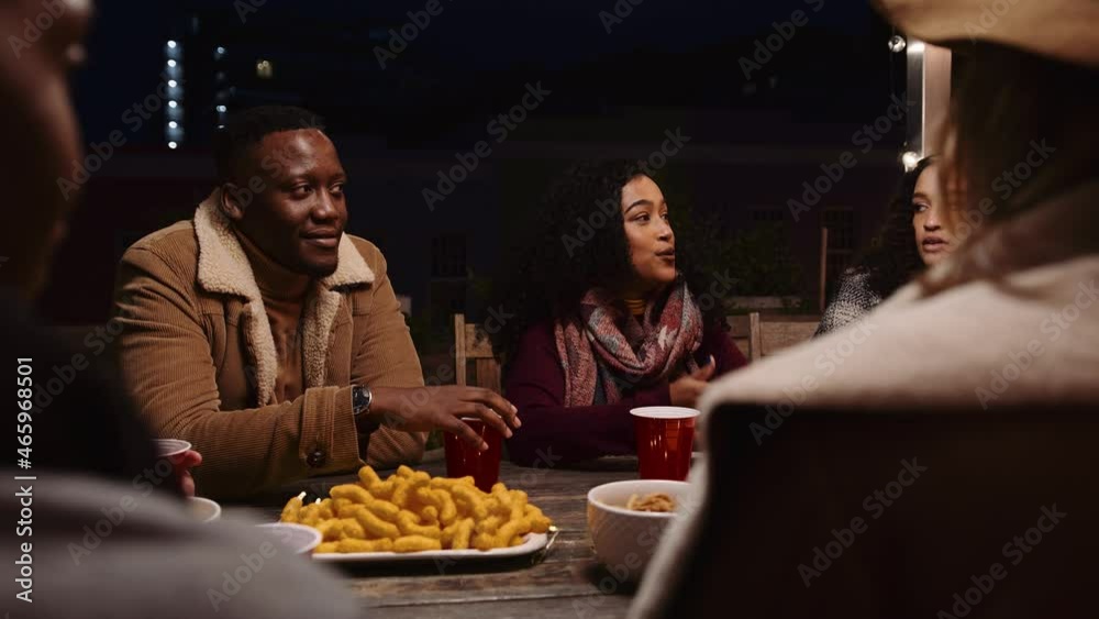 Black male and diverse group of friends chatting, laughing and snacking at a party outdoors at a table Black male and diverse group of friends chatting, laughing and snacking at a party outdoors at a table