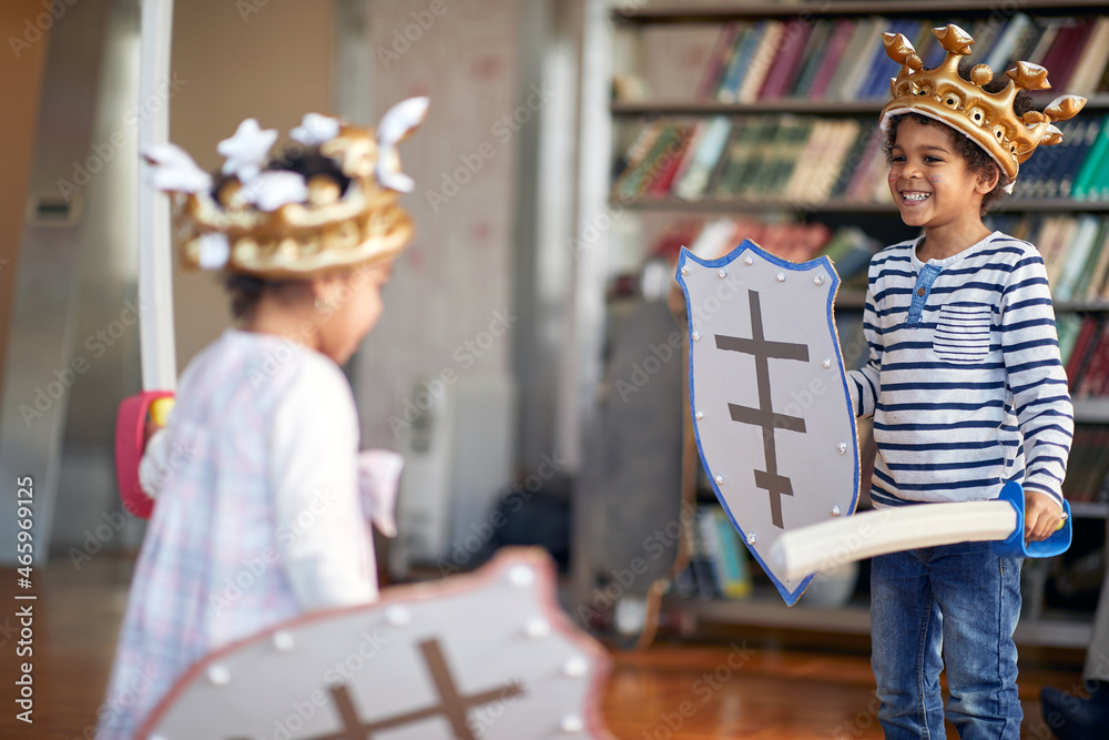 A little brother and sister dressed like knights are ready for swords fight game while playing at home. Family, home, playtime A little brother and sister dressed like knights are ready for swords fight game while playing at home. Family, home, playtime