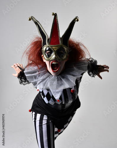 close up portrait of red haired girl wearing a black and white clown jester costume, theatrical circus character. Standing pose isolated on studio background.