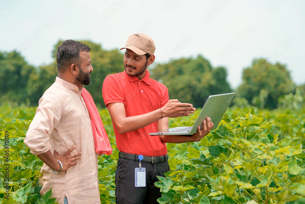 Young indian agronomist showing information to farmer in laptop at green agriculture field. Young indian agronomist showing information to farmer in laptop at green agriculture field.