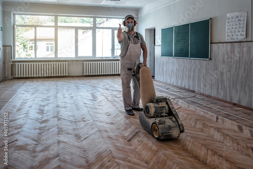 man sands the parquet in the classroom and shows a thumbs up