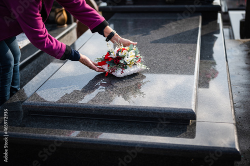 Unrecognizable old woman laying down bouquet of  flowers on a grave. Paying respect at cemetery. photo