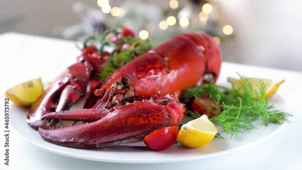 Crop shot of freshly cooked red lobster with vegetables on a plate and white table. Christmas light on a background. Holidays food concept. Handheld footage. 4K, UHD Crop shot of freshly cooked red lobster with vegetables on a plate and white table. Christmas light on a background. Holidays food concept. Handheld footage. 4K, UHD