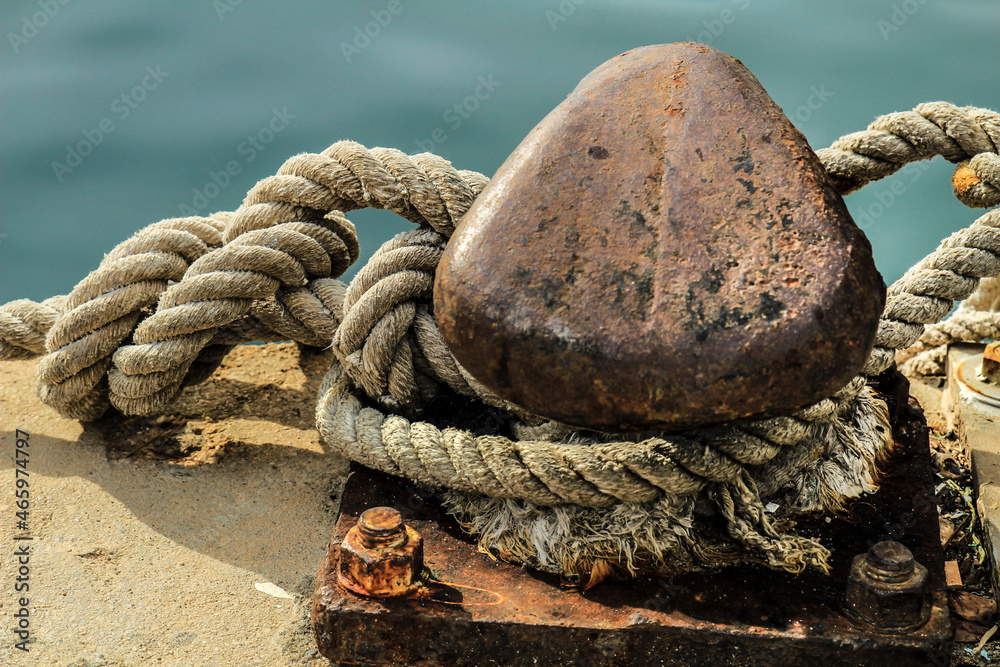 Fototapeta premium Rusty mooring bollard with tied rope in the port