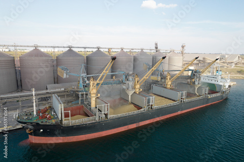 Loading grain into holds of sea cargo vessel through an automatic line in seaport from silos of grain storage. Bunkering of dry cargo ship with grain photo