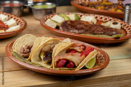Three tacos served on a clay plate accompanied by salsa and lemons on a wooden table