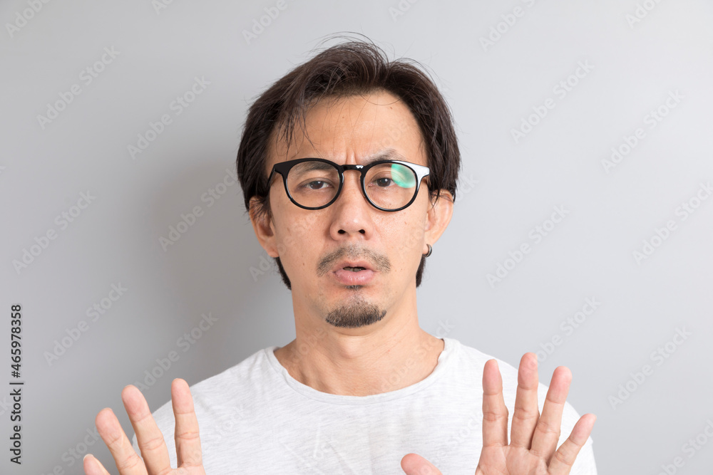 Adult Asian man with eyeglasses raising hand with disagreement on grey background. Adult Asian man with eyeglasses raising hand with disagreement on grey background.
