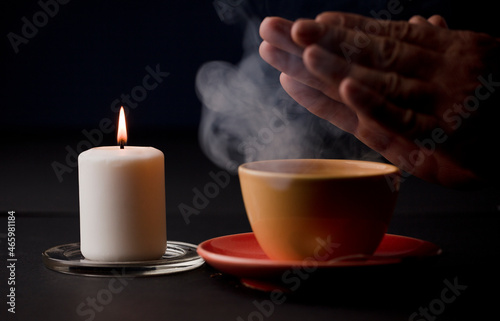 candle with flame  with yellow cup and smoke  hands warming with the heat of the drink   focus on candle 