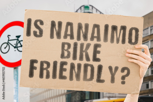 The question " Is Nanaimo bike friendly? " on a banner in men's hand with blurred background. Transportation. Zero waste. Bicycle lane. Streets. City. Safety. Insecure. Road signs. Dangerous