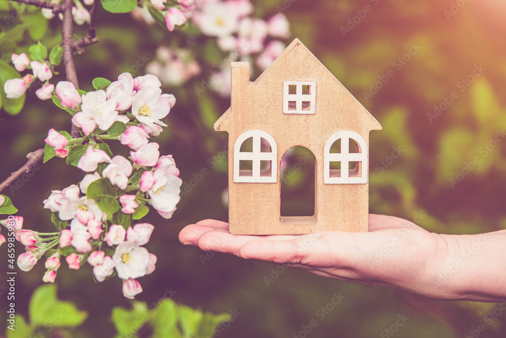 The girl holds the house symbol against the background of blossoming appletree
The girl holds the house symbol against the background of blossoming appletree