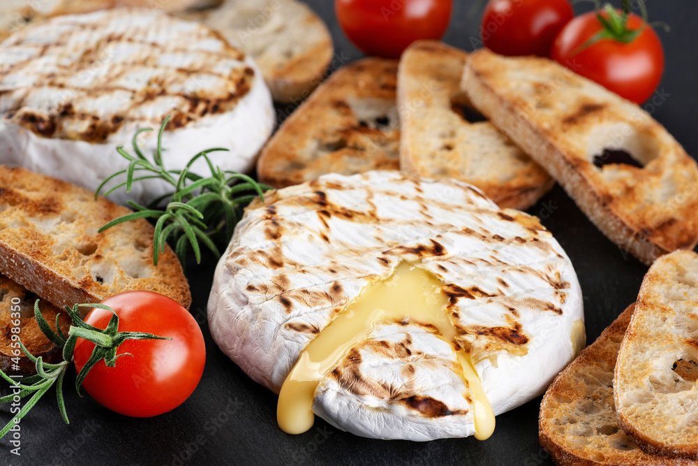 Grilled camembert, brie cheese with croutons, and cherry tomatoes on a dark background.