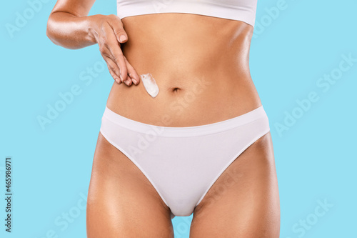 Closeup of young woman apply lotion on her flat belly © Prostock-studio