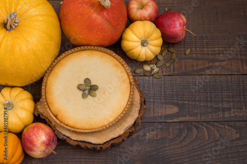 Pumpkin pie on wooden stands surrounded by pumpkins and apples on a dark wooden background.