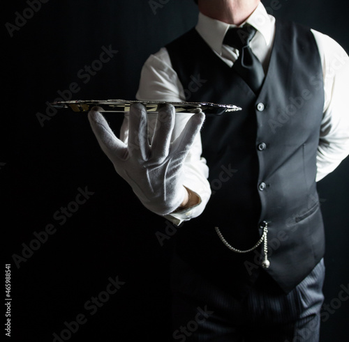 Portrait of Waiter or Butler in White Gloves Holding a Silver Serving Tray on Black Background. Concept of Service Industry and Professional Courtesy.