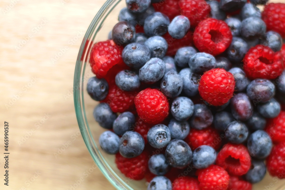 Glass bowl filled with raspberries and blueberries on wooden table. Top view. Glass bowl filled with raspberries and blueberries on wooden table. Top view.