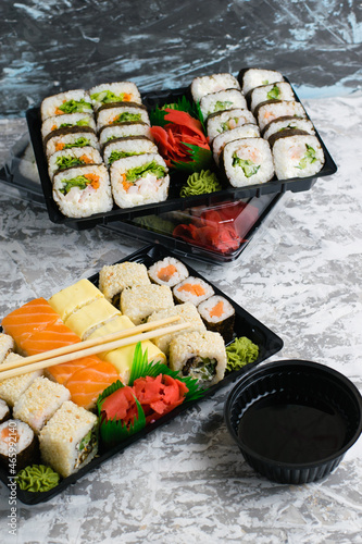 Several sets of sushi with wasabi and soy sauce in plastic packaging on a light gray background. Delicious rolls with shrimp, cucumber and spinach. Food delivery to your home or office.