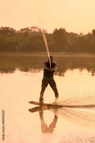 athletic man engaged in water sport and skilfully balancing on water surface on a wakeboard photo