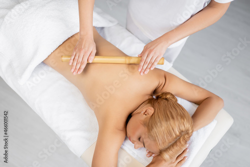 top view of professional masseur massaging back of blonde woman with bamboo stick