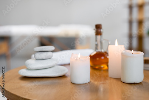 hot stones near jug with massage oil, candles, towel roll and container with cosmetic cream on table