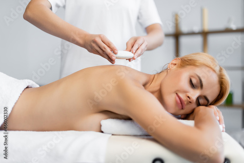 masseur placing hot stone on blonde client in spa center