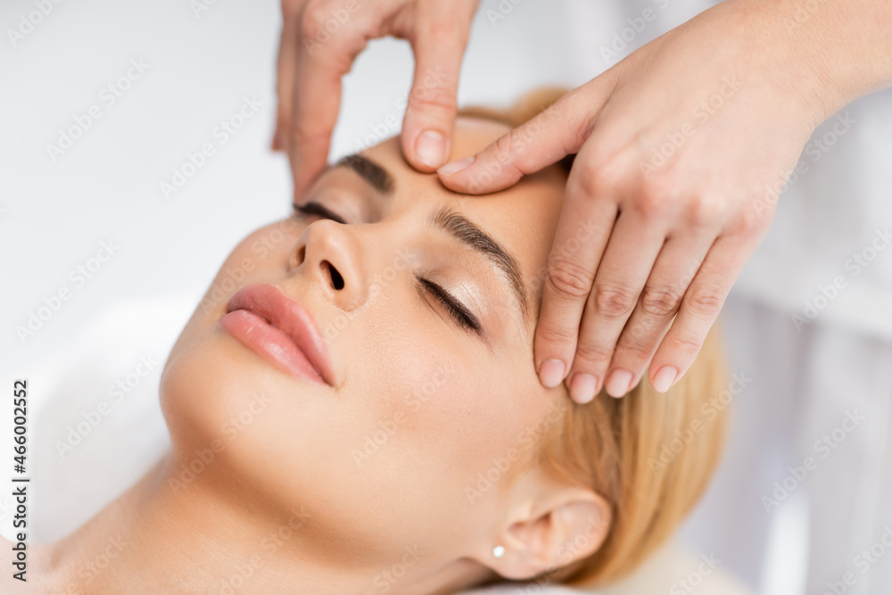 close up of blonde client with closed eyes receiving face massage in spa center