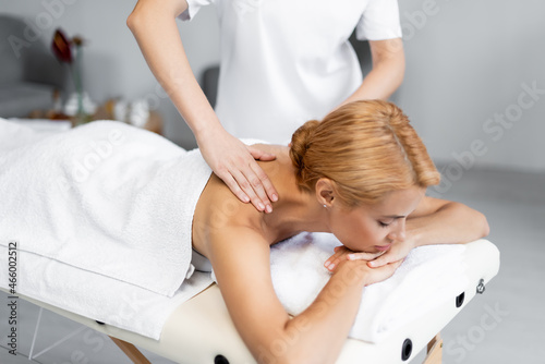 masseur doing shoulder massage to blonde client with closed eyes