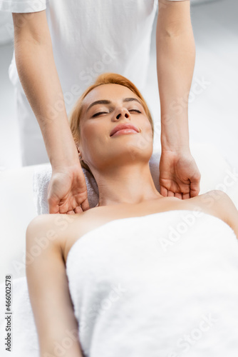 pleased client with closed eyes receiving shoulder massage in spa center