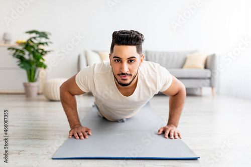Strong young Arab man making strength workout, standing in plank pose at home