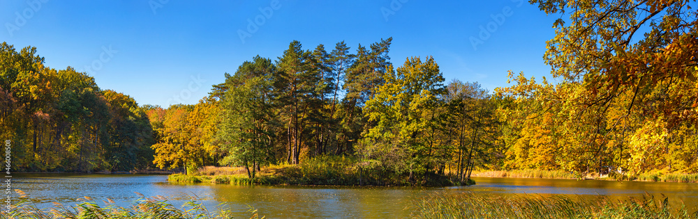 Autumn landscape, panorama, banner - view of a small island on the lake with reflection in the water of autumn trees against a clear blue sky