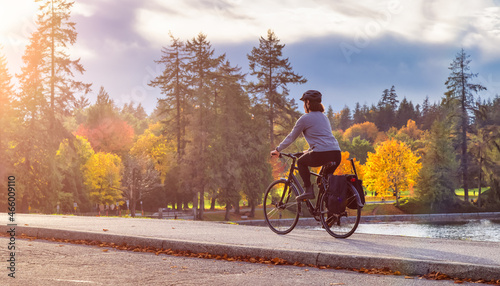 White Caucasian Adult Woman riding a bicycle on Seawall in Stanley Park. Cloudy Fall Season. Downtown Vancouver, BC, Canada.