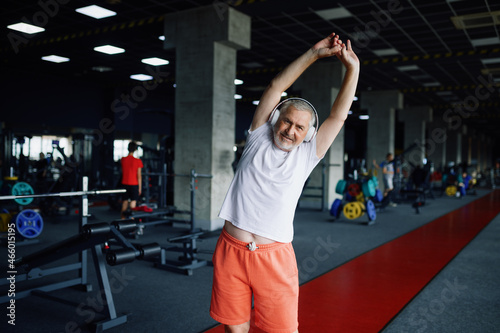 Old man in headphones doing fit exercise, gym