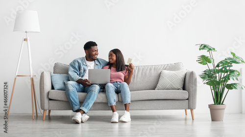 Happy black couple using pc and credit card at home © Prostock-studio