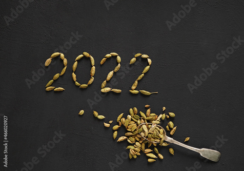 Healthy Food concept Aroma Spice dried Cardamoms in the form of 2022 new year and full spoon on black slate background with copy for text