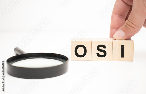 osi text wooden cube blocks and hand holding magnifying glass on table background.