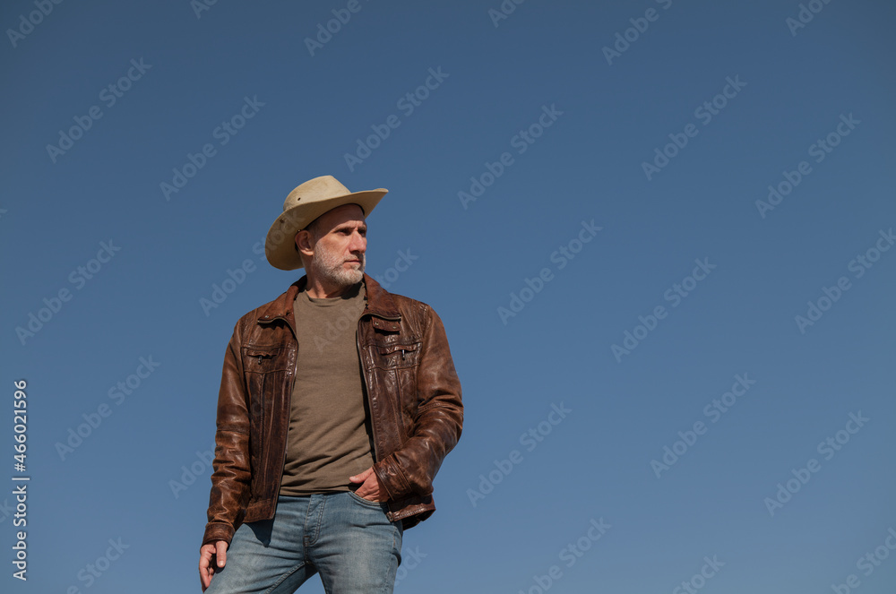 Portrait of adult man with brown leather jacket and cowboy hat against blue clear sky