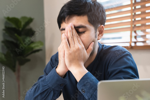 A stressed young man has tired eyes and headache symptoms after looking at the computer display too much.